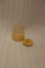 Three ribbed amber glass storage canisters with wooden lids and crystal knobs sitting on a marble kitchen countertop.
