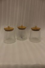 Three ribbed glass storage jars with natural wooden lids topped with clear crystal diamond knobs on a kitchen countertop.