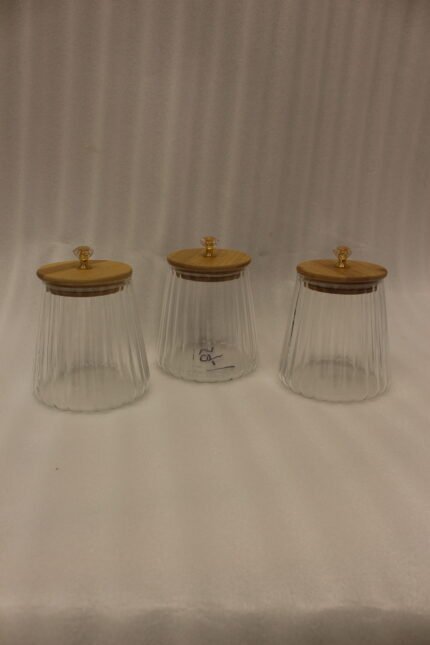 Three ribbed glass storage jars with natural wooden lids topped with clear crystal diamond knobs on a kitchen countertop.