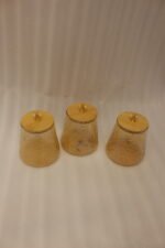 Three amber textured glass storage jars with natural wooden lids and crystal crystal-cut handles sitting on a marble kitchen countertop.