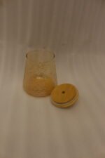 Three amber textured glass storage jars with natural wooden lids and crystal crystal-cut handles sitting on a marble kitchen countertop.