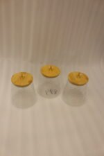 Three hammered glass kitchen storage jars with wooden wooden lids and crystal handles on a white marble countertop