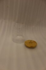 Three hammered glass kitchen storage jars with wooden wooden lids and crystal handles on a white marble countertop