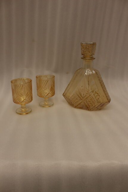 Amber crystal glass bottle and matching stemmed glasses set with diamond pattern on a marble table