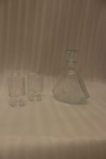Crystal glass water bottle decanter with stopper alongside matching patterned stemmed glasses on a kitchen counter.