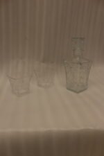 Clear crystal glass decanter bottle and matching tumbler drinking glasses with diamond pattern on kitchen counter