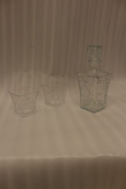Clear crystal glass decanter bottle and matching tumbler drinking glasses with diamond pattern on kitchen counter