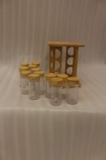 Square wooden bamboo spice rack holding 12 clear glass seasoning jars with wooden lids on a kitchen countertop