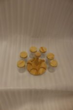 Six clear glass spice jars with smooth wooden lids arranged on a revolving wooden carousel stand on a kitchen countertop.