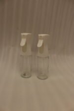 2 Pcs clear glass oil sprayer bottle set with ergonomic white trigger nozzles on a kitchen countertop