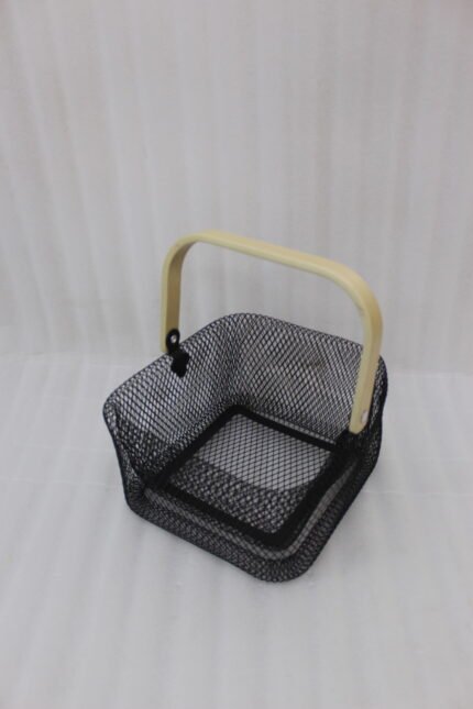 Black double-wall wire mesh storage basket with a wooden top handle sitting on a marble kitchen countertop