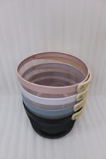 Stacked round metal wire mesh storage baskets with wooden handles in dusky pink, white, grey, and black on a marble countertop.