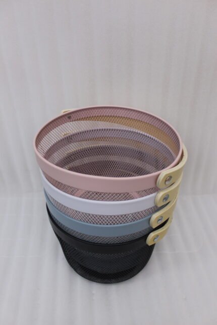 Stacked round metal wire mesh storage baskets with wooden handles in dusky pink, white, grey, and black on a marble countertop.
