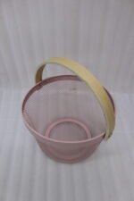 Stacked round metal wire mesh storage baskets with wooden handles in dusky pink, white, grey, and black on a marble countertop.