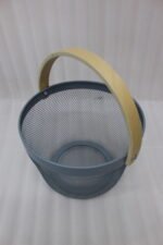 Stacked round metal wire mesh storage baskets with wooden handles in dusky pink, white, grey, and black on a marble countertop.