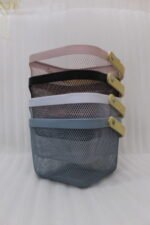 Stack of modern mesh wire storage baskets in pink, black, white, and blue with light wooden handles on a kitchen countertop.
