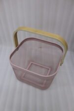 Stack of modern mesh wire storage baskets in pink, black, white, and blue with light wooden handles on a kitchen countertop.