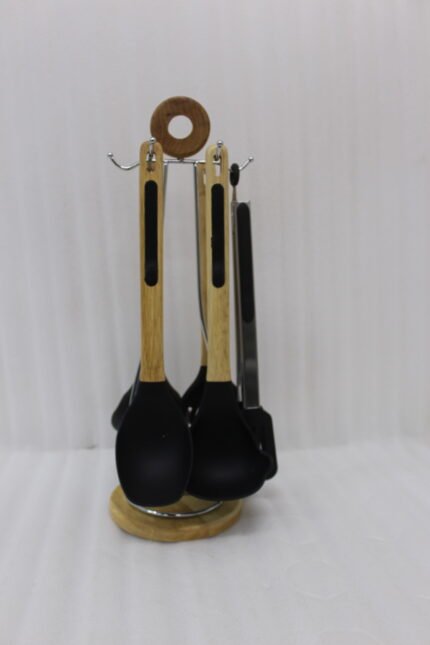 7-piece black silicone cooking utensil set with wooden handles on a rotating stand sitting on a marble kitchen countertop.