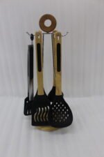 7-piece black silicone cooking utensil set with wooden handles on a rotating stand sitting on a marble kitchen countertop.