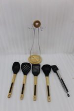 7-piece black silicone cooking utensil set with wooden handles on a rotating stand sitting on a marble kitchen countertop.