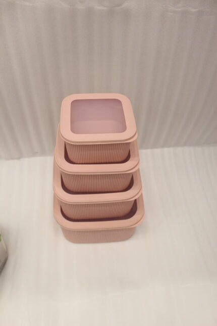 Four dusty rose ribbed plastic storage boxes with lids stacked vertically by size on a white marble kitchen countertop