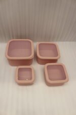 Four dusty rose ribbed plastic storage boxes with lids stacked vertically by size on a white marble kitchen countertop