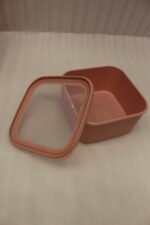 Four dusty rose ribbed plastic storage boxes with lids stacked vertically by size on a white marble kitchen countertop