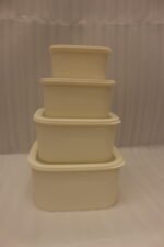 Stacked set of four cream-colored fluted plastic storage boxes with lids on a white kitchen countertop.