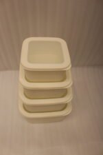Stacked set of four cream-colored fluted plastic storage boxes with lids on a white kitchen countertop.