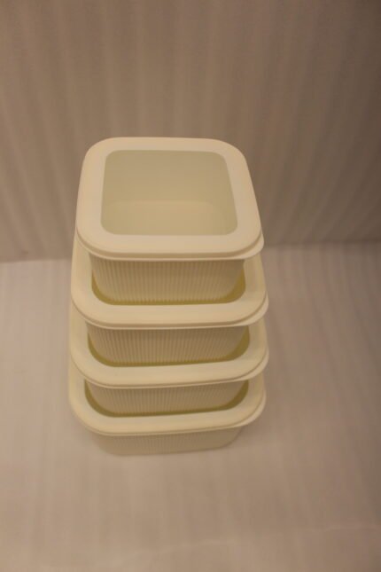 Stacked set of four cream-colored fluted plastic storage boxes with lids on a white kitchen countertop.