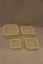 Stacked set of four cream-colored fluted plastic storage boxes with lids on a white kitchen countertop.