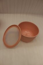 Stack of three dusty pink ribbed plastic food storage bowls with clear lids on a white kitchen countertop.