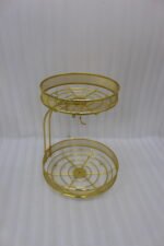 Two-tier round gold wire fruit basket holder with mesh borders and integrated banana hanger hook sitting on a wooden tabletop.
