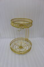 Two-tier round gold wire fruit basket holder with mesh borders and integrated banana hanger hook sitting on a wooden tabletop.
