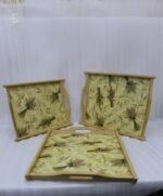 Set of three rectangular wooden serving trays with wheat botanical pattern and handles resting on a marble kitchen countertop.