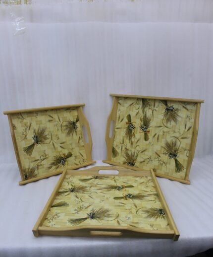 Set of three rectangular wooden serving trays with wheat botanical pattern and handles resting on a marble kitchen countertop.