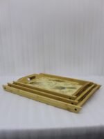 Set of three rectangular wooden serving trays with wheat botanical pattern and handles resting on a marble kitchen countertop.