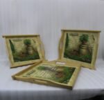 Set of three rectangular natural wooden serving trays with side handles featuring a printed rustic garden scene resting on a marble kitchen countertop.