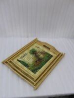 Set of three rectangular natural wooden serving trays with side handles featuring a printed rustic garden scene resting on a marble kitchen countertop.