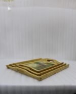 Set of three rectangular natural wooden serving trays with side handles featuring a printed rustic garden scene resting on a marble kitchen countertop.