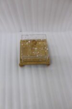 Modern square wooden cake dish with a clear acrylic lid featuring embedded silver leaf flakes and round wooden feet on a marble countertop.