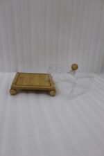 Modern square wooden cake dish with a clear acrylic lid featuring embedded silver leaf flakes and round wooden feet on a marble countertop.
