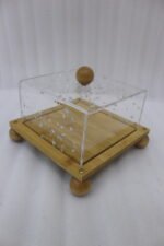 Modern square wooden cake dish with a clear acrylic lid featuring embedded silver leaf flakes and round wooden feet on a marble countertop.