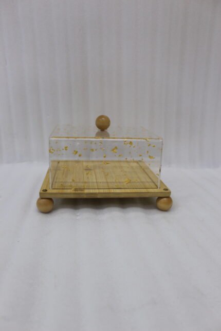 Square bamboo cake stand with gold flecked acrylic dome cover set on a kitchen counter