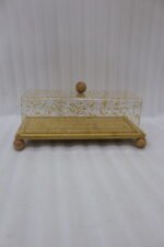Rectangular wooden cake display tray with a gold flake patterned acrylic cover and wooden ball feet on a marble countertop