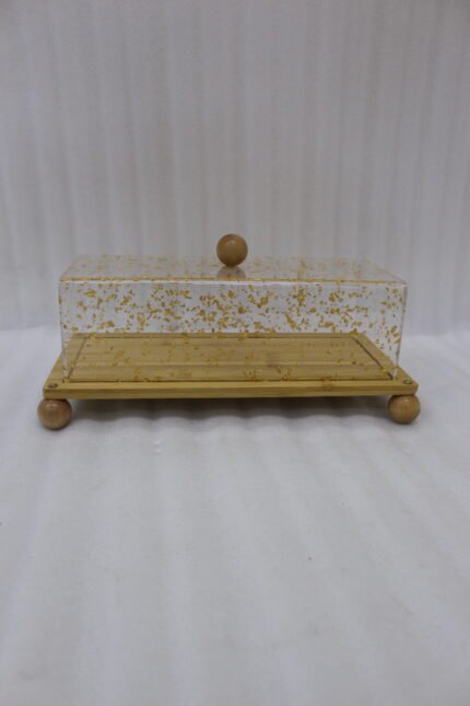 Rectangular wooden cake display tray with a gold flake patterned acrylic cover and wooden ball feet on a marble countertop