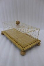 Rectangular wooden cake display tray with a gold flake patterned acrylic cover and wooden ball feet on a marble countertop