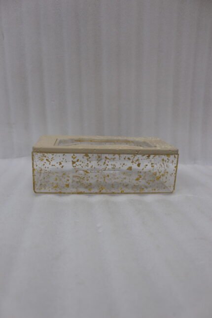 Clear acrylic tissue box holder embedded with gold flakes and a textured beige lid sitting on a wooden table