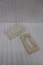 Clear acrylic tissue box holder embedded with gold leaf flakes and topped with a textured light gold lid on a wooden coffee table.