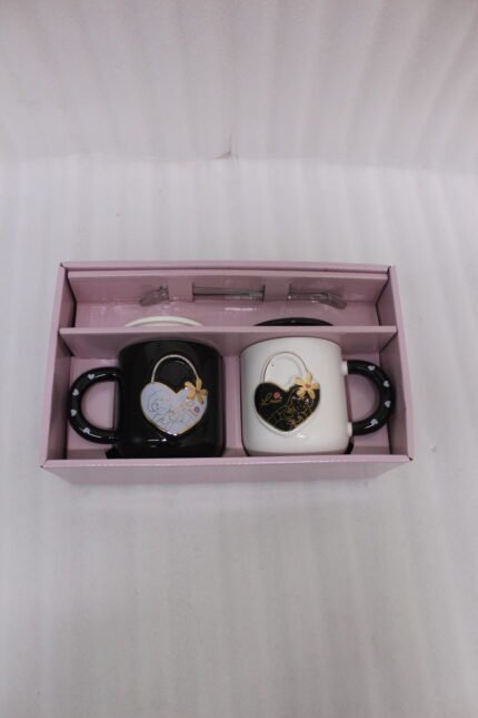 Pair of black and white ceramic couple mugs with heart accents, matching lids, and silver spoons sitting on a kitchen countertop.